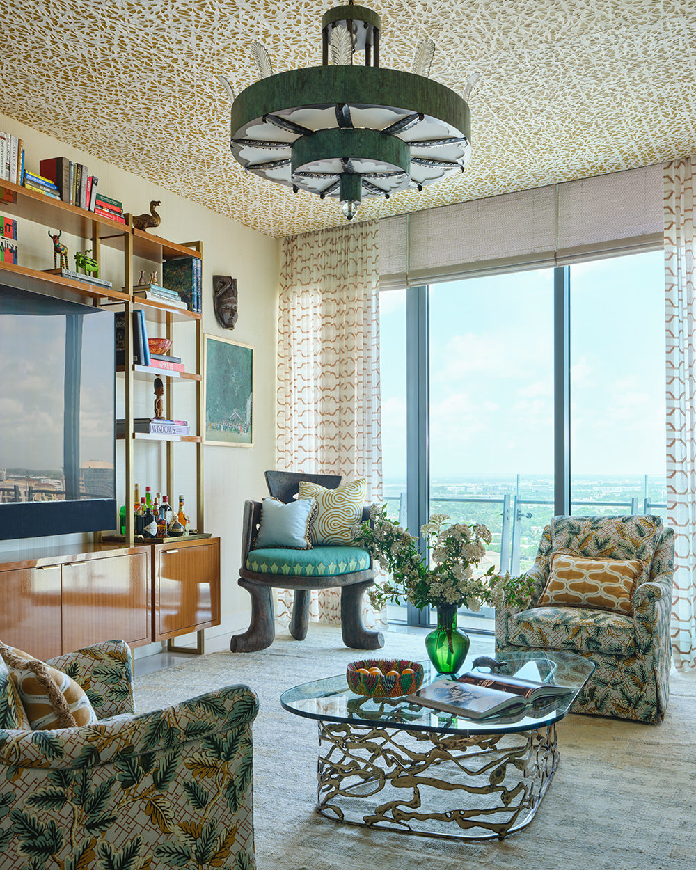 Study with a woven ceiling, brass shelving, a green upholstered bench and leaf print armchairs by the window
