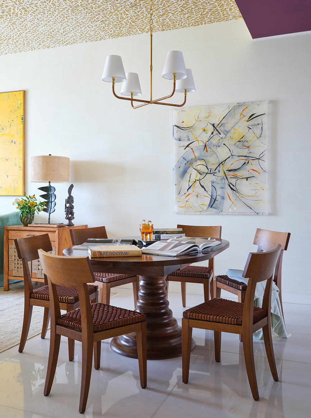 Dining corner with a woven ceiling, a round timber table with caned chairs and a pale abstract canvas