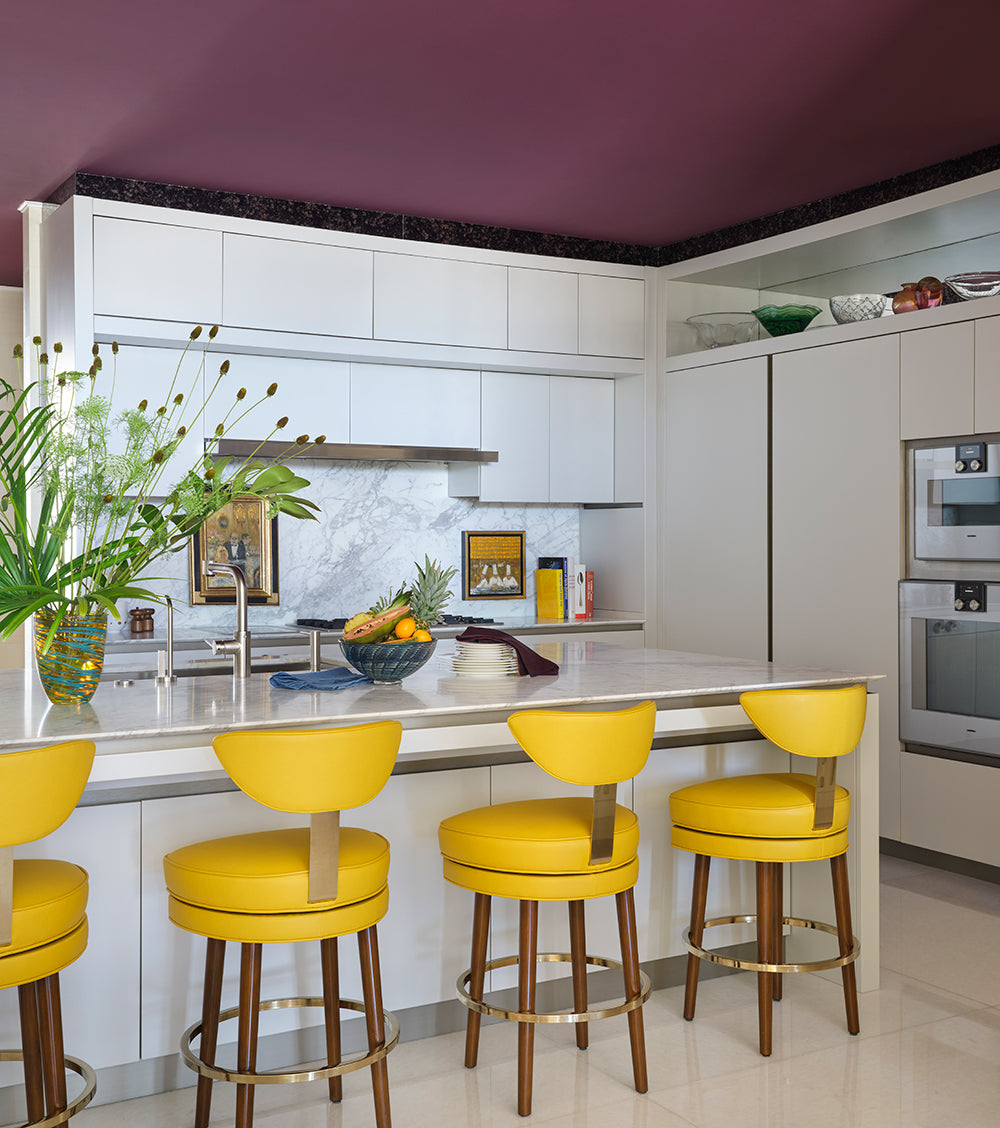 White kitchen with a plum ceiling, yellow leather bar stools and a marble splashback
