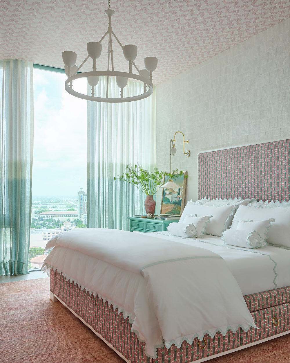 Bedroom with a pink basketweave headboard, sheer green curtains and a city view