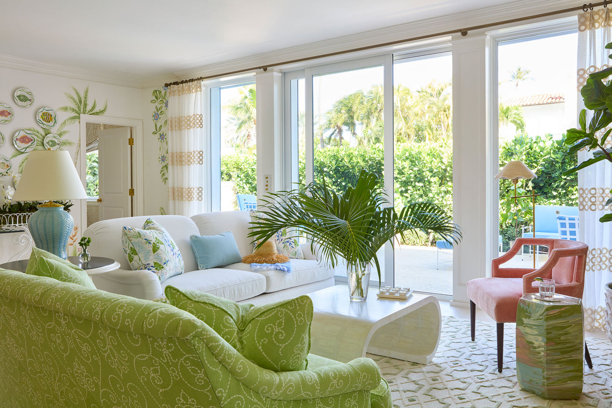 Living room with green damask sofas, a wall of glass to the terrace and a potted palm