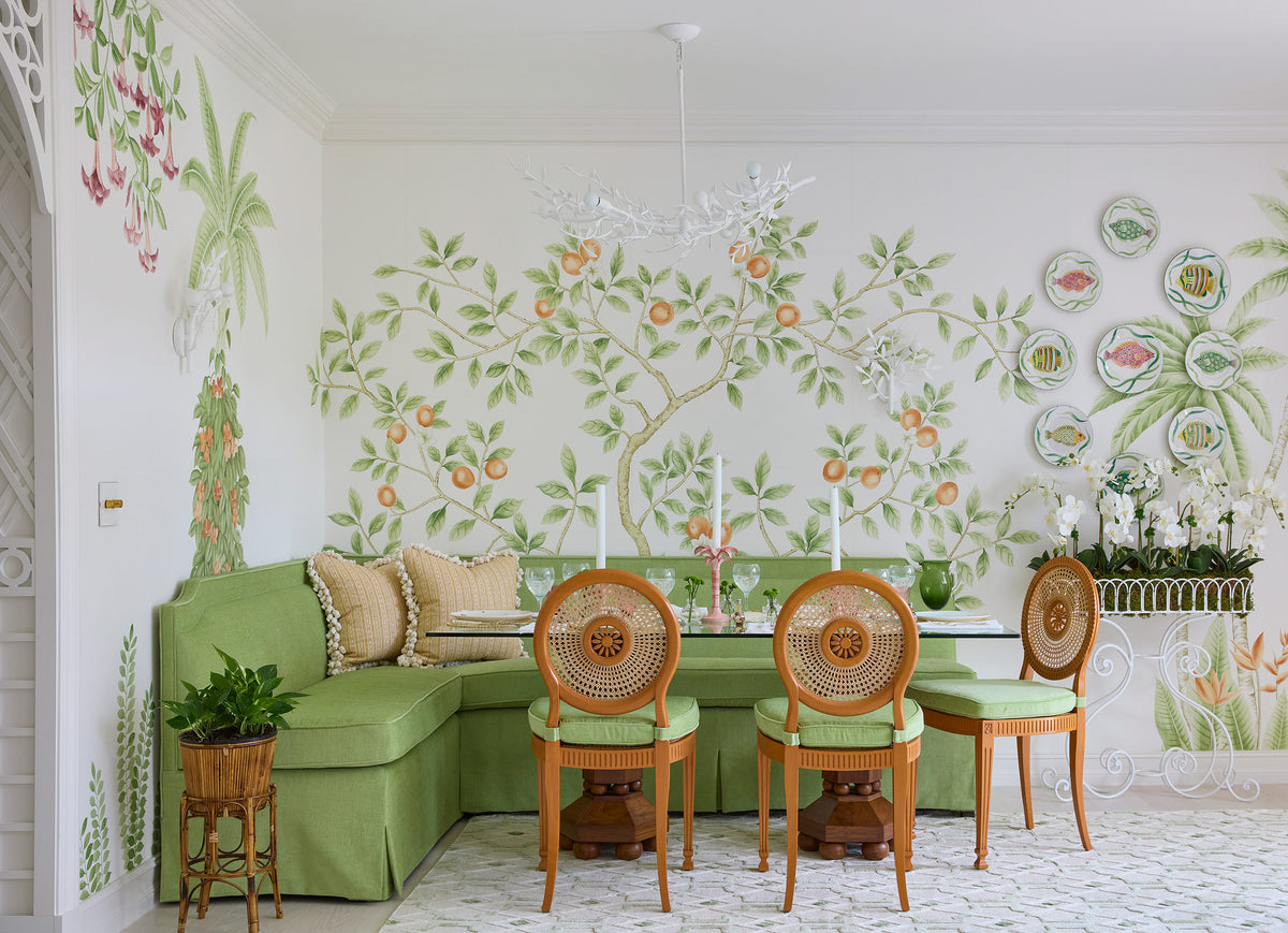Breakfast room hand painted with flowering trees, a green banquette, caned chairs and a wall of decorative plates