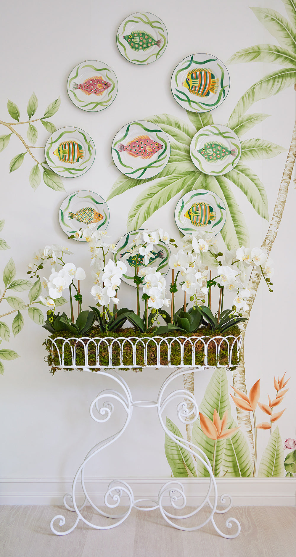 Hand painted palm mural hung with fish plates above a white scrolled planter of orchids