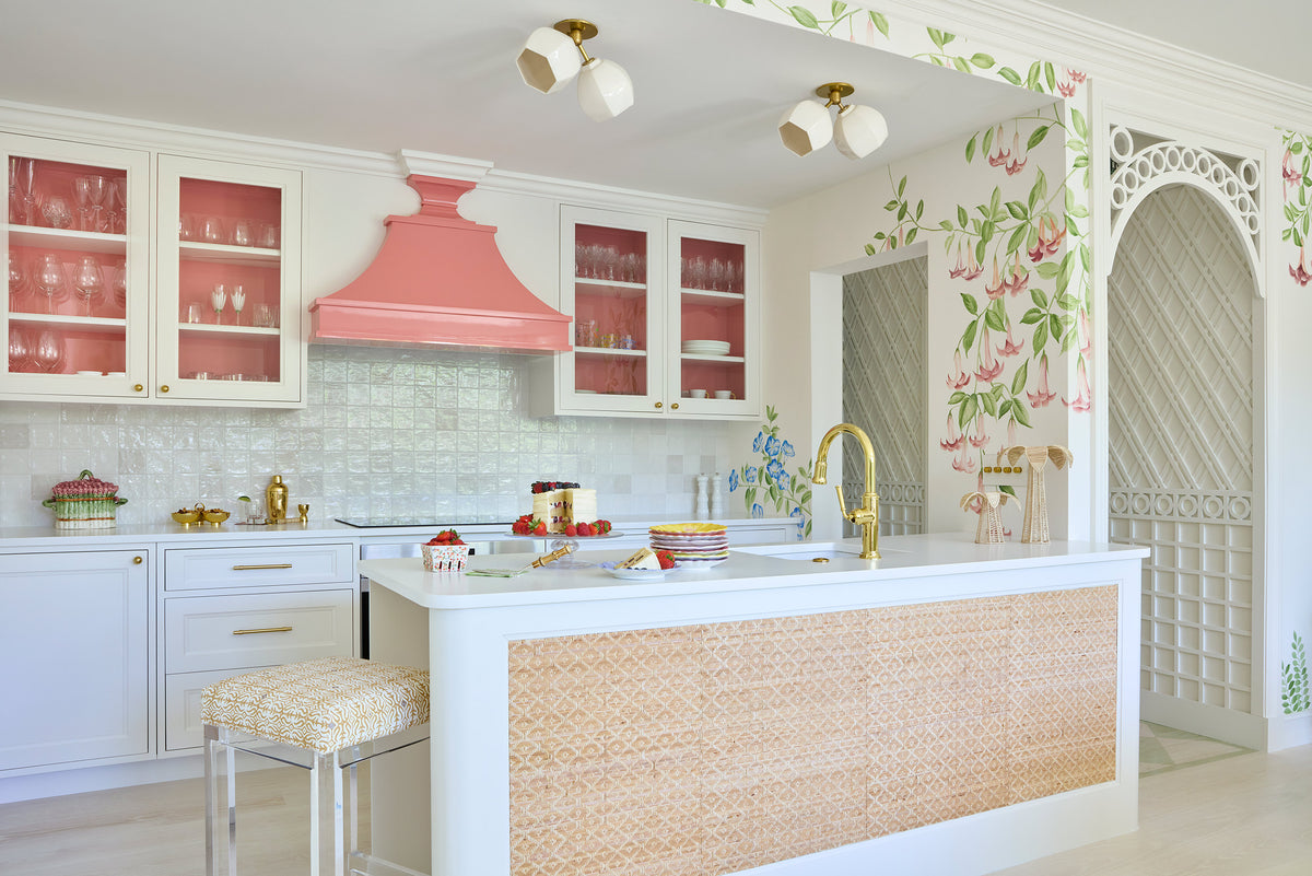 Kitchen with a coral range hood, glazed cabinets, a caned island and a painted trellis beyond