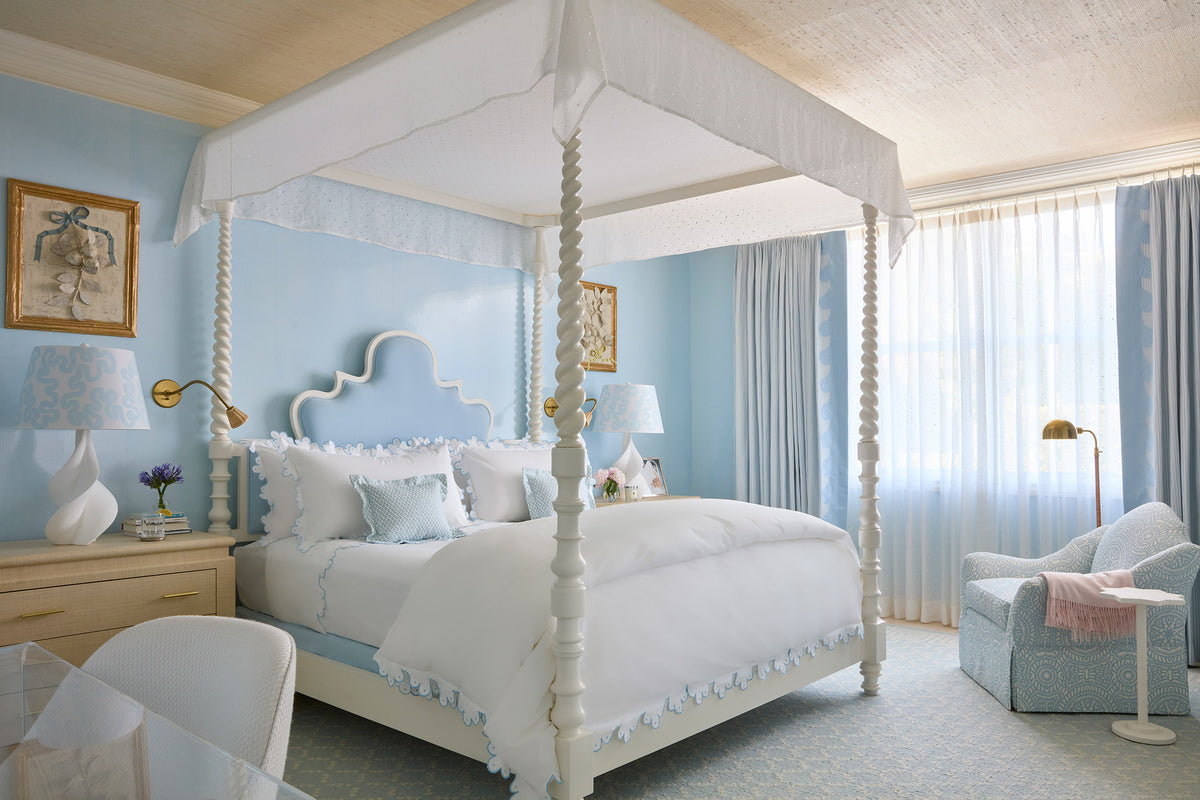 Bedroom with a white four poster, pale blue walls, a scalloped headboard and a bow framed print