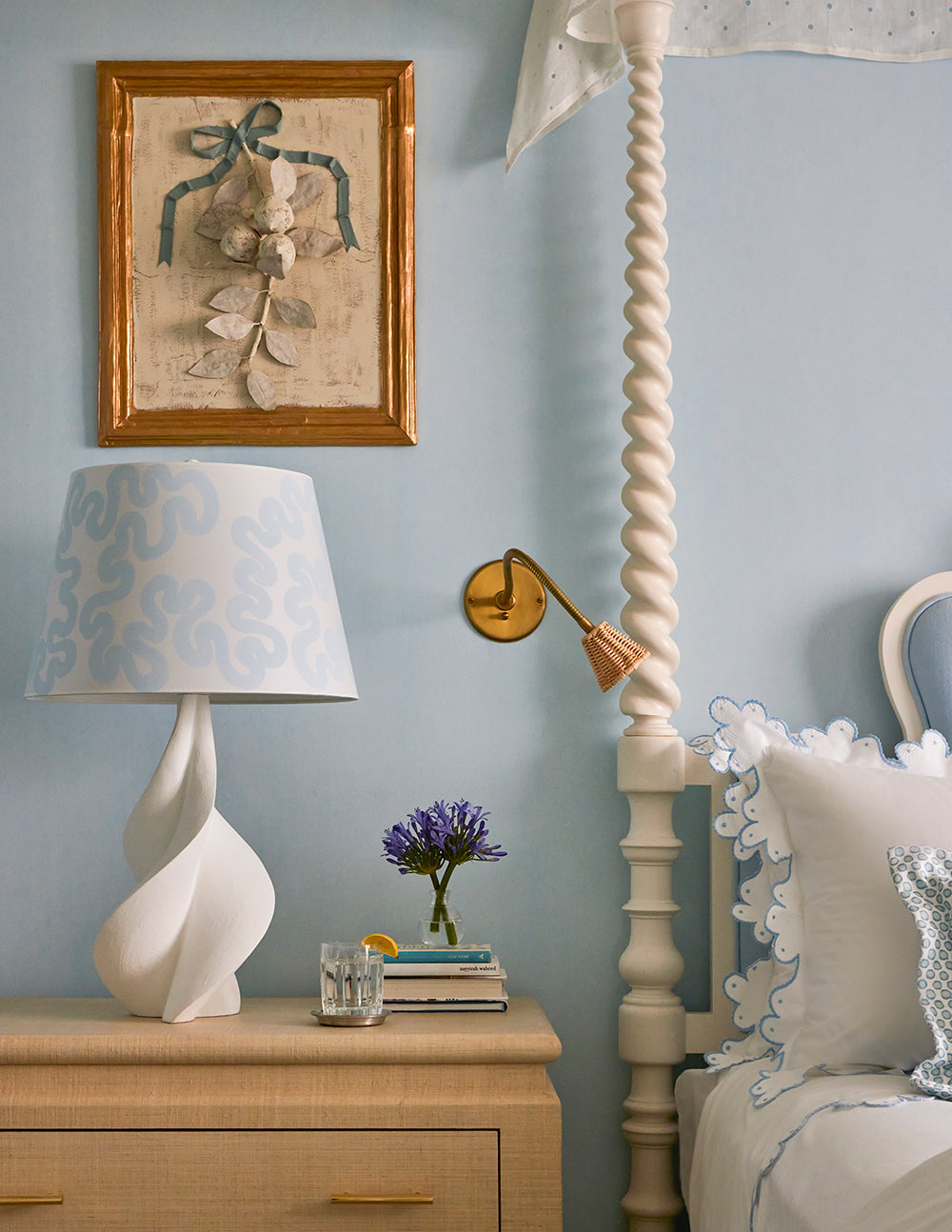 Bedside detail with a sculptural white lamp, a bow framed print and lavender on a limed chest