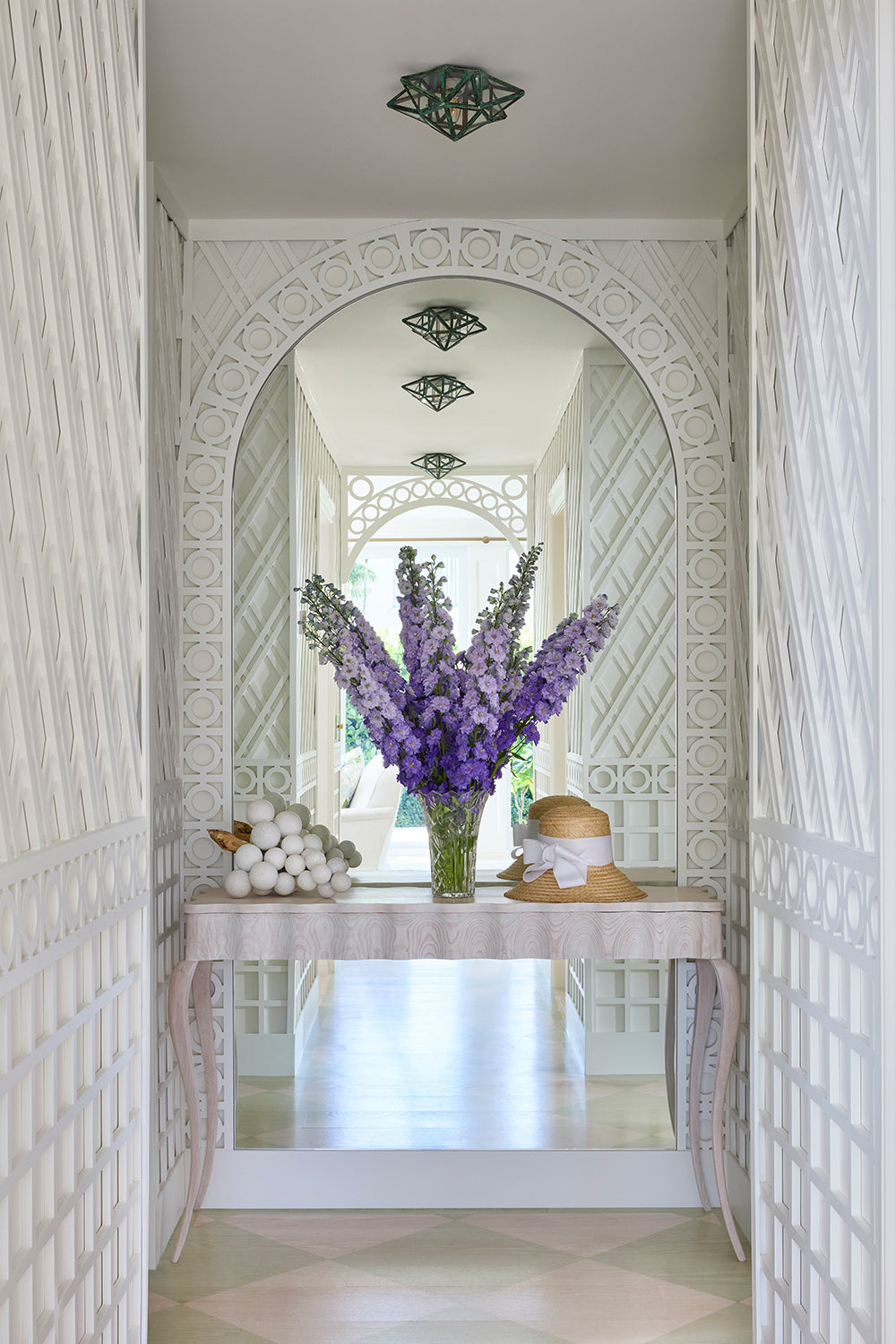 Arched trellis hall with a skirted console and a tall vase of delphiniums